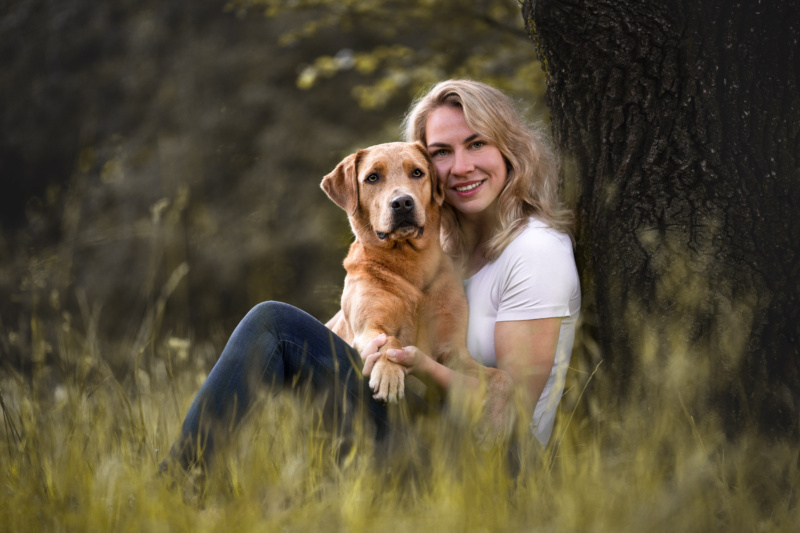 Labrador und Frauchen sitzen im Gras angelehnt an einen Baum