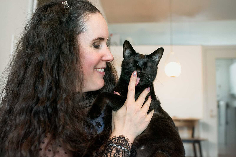Eine schwarze Katze leckt ihrer lachenden Besitzerin liebevoll über die Nase, aufgenommen bei einem entspannten Fotoshooting zu Hause in Luzern.