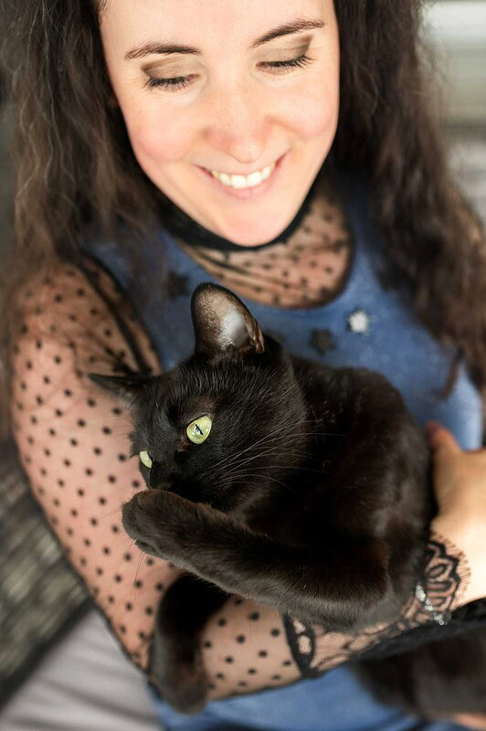 Eine lächelnde Frau hält ihre schwarze Katze mit leuchtend grünen Augen liebevoll im Arm während eines entspannten Fotoshootings zu Hause in Luzern.