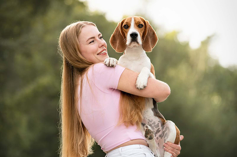 Eine glückliche Besitzerin hält ihren Beagle auf dem Arm bei einem Hundefotoshooting im Spätsommer an der Emme, in der Region Bern / Solothurn.