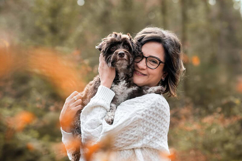 Eine glückliche Frau hält ihren braunen Bolonka Zwetna liebevoll im Arm und lächelt, aufgenommen bei einem Herbst-Shooting im Wald bei Deitingen (Solothurn).