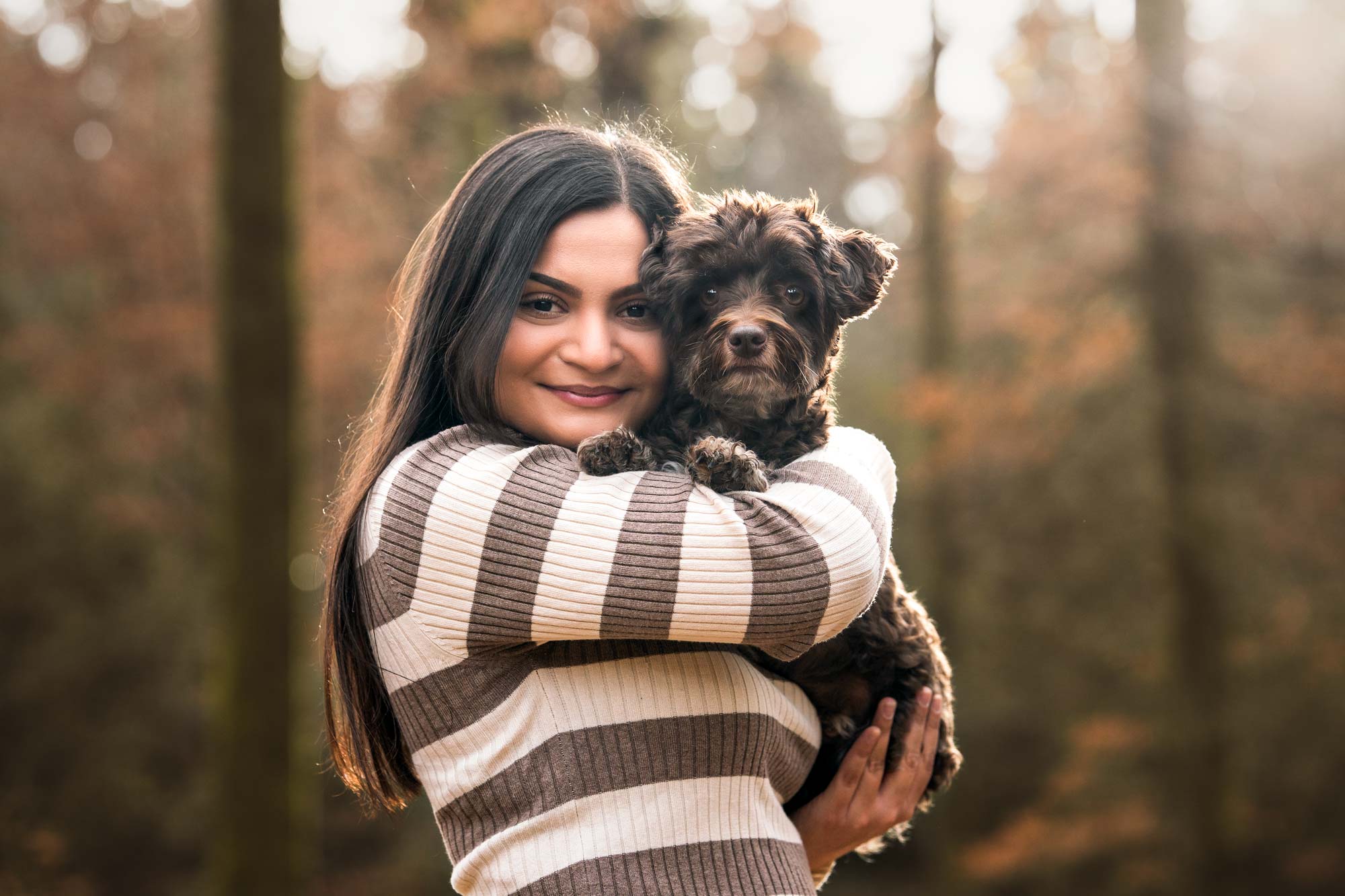 Dein Hundefotoshooting Paket: Bilder mit Herz Eine glückliche Frau hält ihren kleinen braunen Bolonka liebevoll auf dem Arm. Entspanntes Hundefotoshooting in der Natur bei Bern und Solothurn.